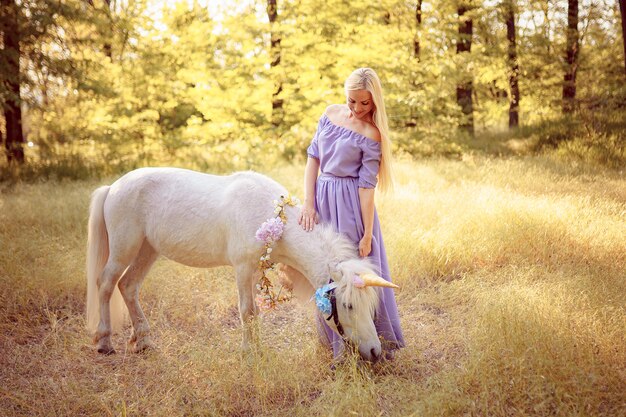 Femme blonde en robe violette étreignant la licorne blanche