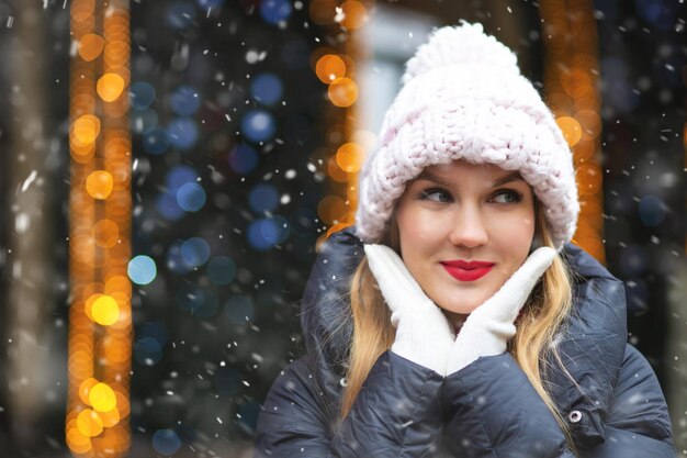 Une femme blonde romantique porte un bonnet en tricot marchant à la foire d'hiver pendant les chutes de neige. Espace vide pour le texte