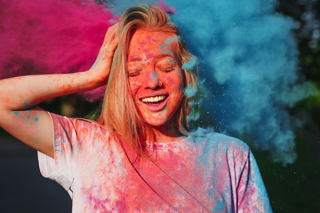 Femme blonde s'amusant avec l'explosion de poudre sèche bleue et rose célébrant le festival Holi