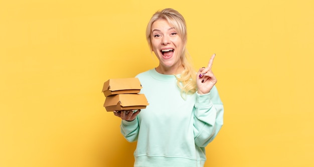 Femme blonde se sentant comme un génie heureux et excité après avoir réalisé une idée, levant joyeusement le doigt, eureka!