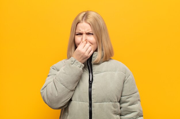 Femme blonde se sentant dégoûtée, tenant le nez pour éviter de sentir une odeur nauséabonde et désagréable