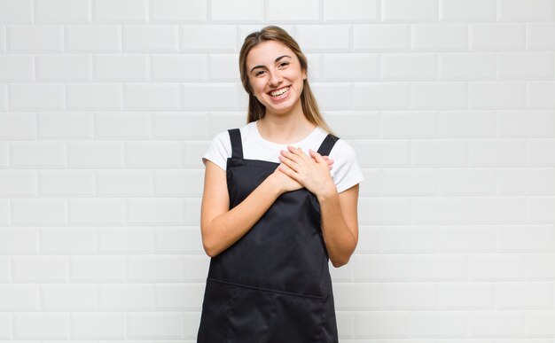 Femme blonde se sentir romantique, heureuse et amoureuse, souriant joyeusement et tenant les mains près du cœur