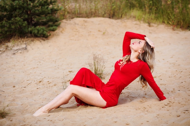 Femme blonde sensuelle en robe rouge sur le sable. Femme posant sur la plage à l'extérieur en été.