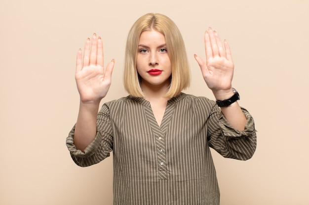 Femme blonde à la sérieuse, malheureuse, en colère et mécontente d'interdire l'entrée ou de dire arrêter avec les deux paumes ouvertes