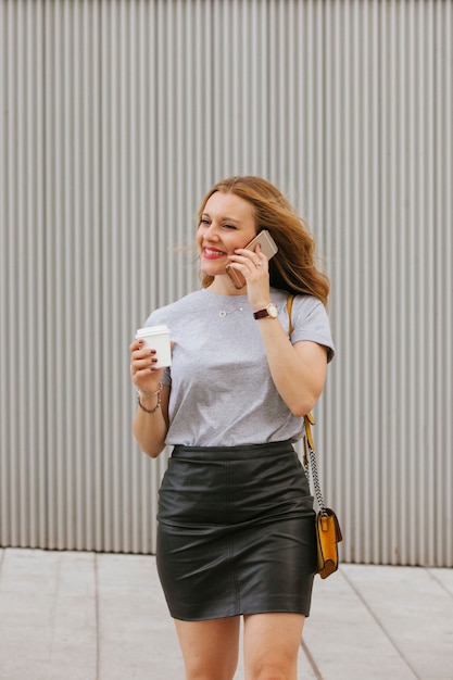 Femme blonde sexy parlant à son téléphone tout en buvant du café