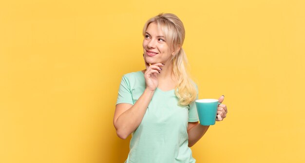 Femme blonde souriant joyeusement et rêvant ou doutant, regardant sur le côté