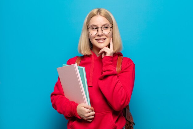 Femme blonde souriant joyeusement et rêvassant ou doutant, regardant sur le côté