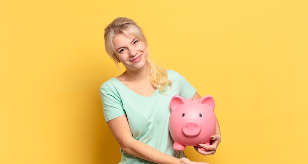 Femme blonde souriant joyeusement, se sentant heureuse et montrant un concept dans l'espace de copie avec la paume de la main