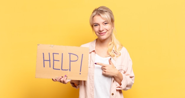 Femme blonde souriant joyeusement, se sentant heureuse et pointant vers le côté et vers le haut, montrant l'objet dans l'espace de copie