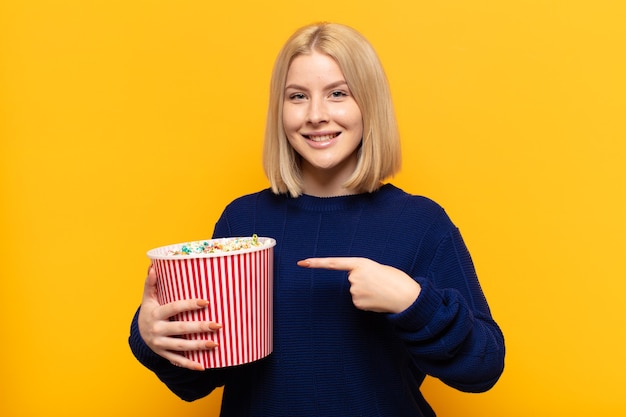 Femme blonde souriant joyeusement, se sentant heureux et pointant vers le côté et vers le haut, montrant l'objet dans l'espace de copie