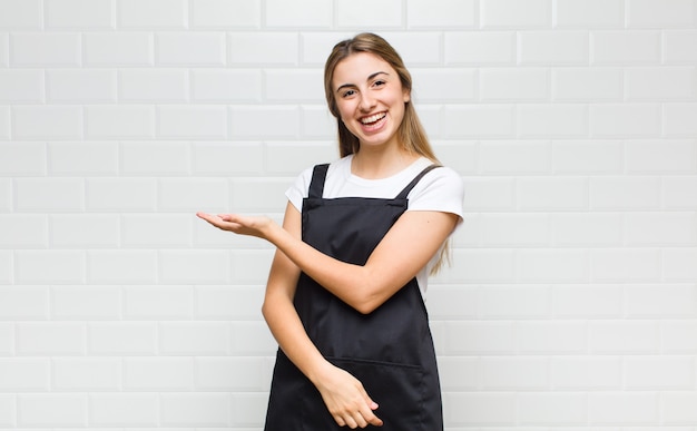 Femme blonde souriant joyeusement, se sentir heureux et montrant un concept dans l'espace de copie avec la paume de la main