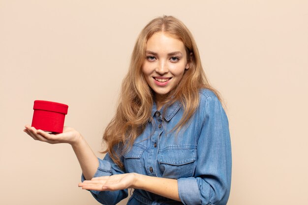 Femme blonde souriant joyeusement, se sentir heureux et montrant un concept dans l'espace de copie avec la paume de la main