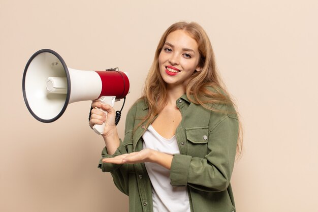 Femme blonde souriant joyeusement, se sentir heureux et montrant un concept dans l'espace de copie avec la paume de la main