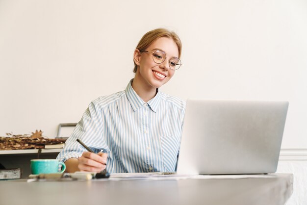 femme blonde souriante architecte à lunettes travaillant avec un ordinateur portable lors de la conception d'un projet sur le lieu de travail