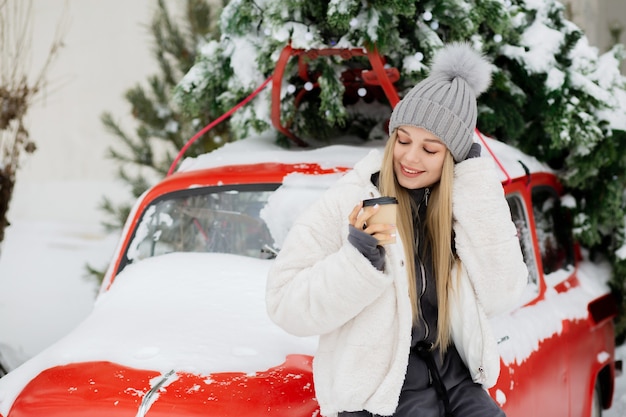 Une femme blonde souriante boit du café au parc d'hiver