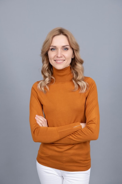 femme blonde souriante a croisé les mains. la beauté féminine et la mode. style décontracté. fille a les cheveux bouclés. style de mode de tous les jours. dame souriante sur fond gris.