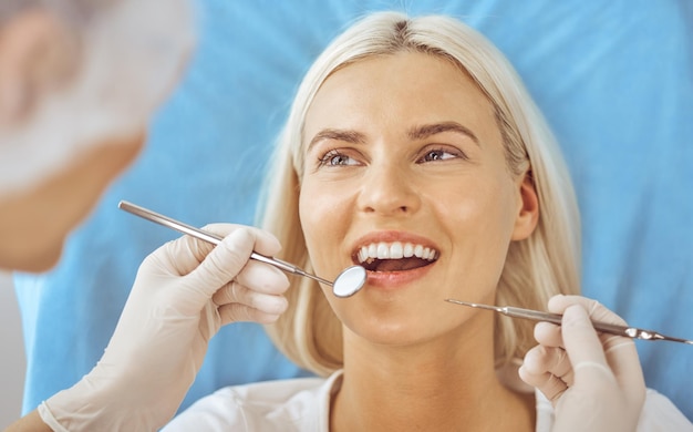 Femme blonde souriante examinée par un dentiste à la clinique dentaire. Dents saines et concept de médecine.