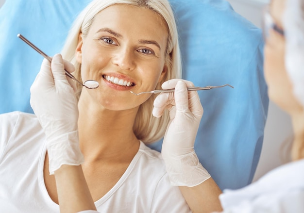 Femme blonde souriante examinée par un dentiste à la clinique dentaire. Dents saines et concept de médecine.