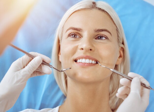 Une femme blonde souriante examinée par un dentiste à la clinique dentaire ensoleillée.