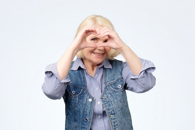 Femme blonde souriante montre le geste du cœur