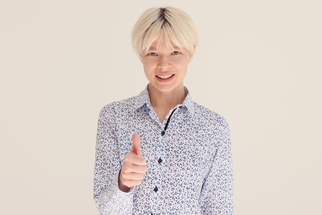 Une femme blonde souriante montre un signe d'approbation au mur