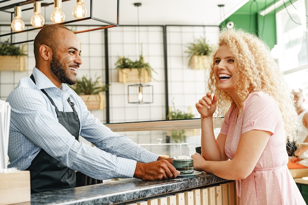 Photo femme blonde souriante parlant à un serveur d'un café au comptoir