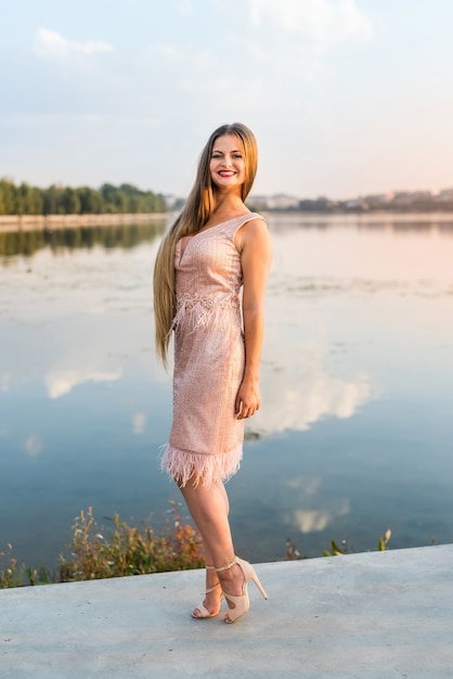 Femme blonde souriante posant en robe de mode sur la plage