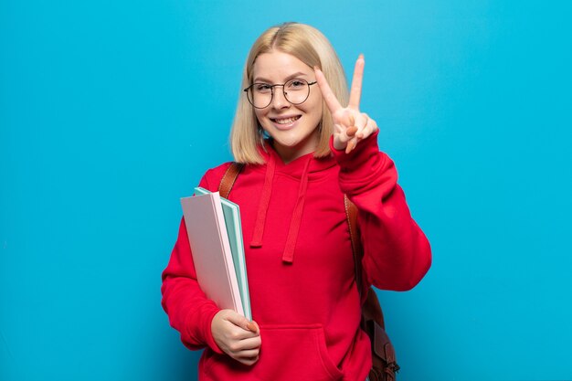 Femme blonde souriante et à la recherche heureuse, insouciante et positive, gesticulant la victoire ou la paix d'une seule main