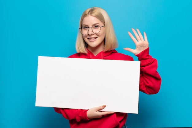 Femme blonde souriante et semblant amicale, montrant le numéro cinq ou cinquième avec la main vers l'avant, compte à rebours