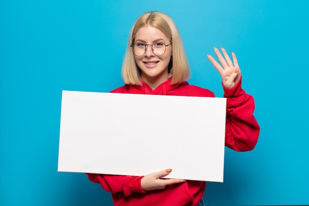 Femme blonde souriante et à la sympathique, montrant le numéro quatre ou quatrième avec la main en avant, compte à rebours