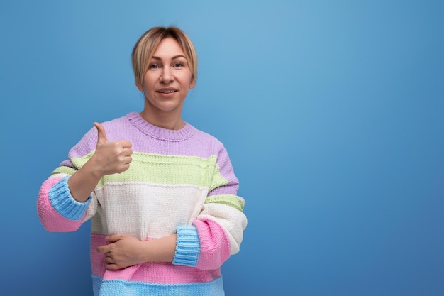 Femme blonde souriante en tenue décontractée montrant comme sur fond bleu avec espace de copie