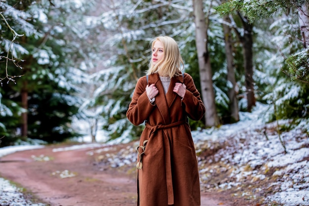 Femme blonde de style en manteau dans la forêt de neige