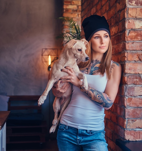 Une femme blonde tatouée élégante en t-shirt et jeans tient un chien mignon.