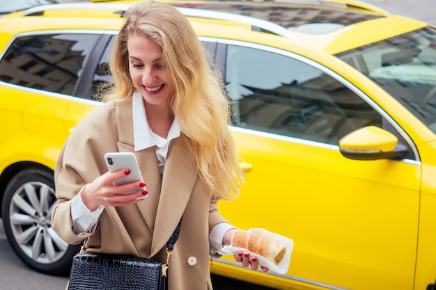 Une femme blonde avec un téléphone dans une rue d'une ville européenne mangeant du trdlo à praha.