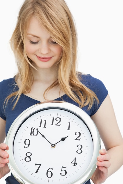 Femme blonde tenant une horloge en souriant