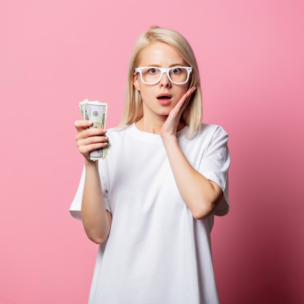 Femme blonde en tshirt blanc et lunettes avec de l'argent sur rose