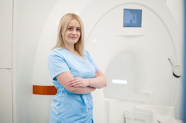 Femme blonde en uniforme bleu debout près de l'appareil IRM