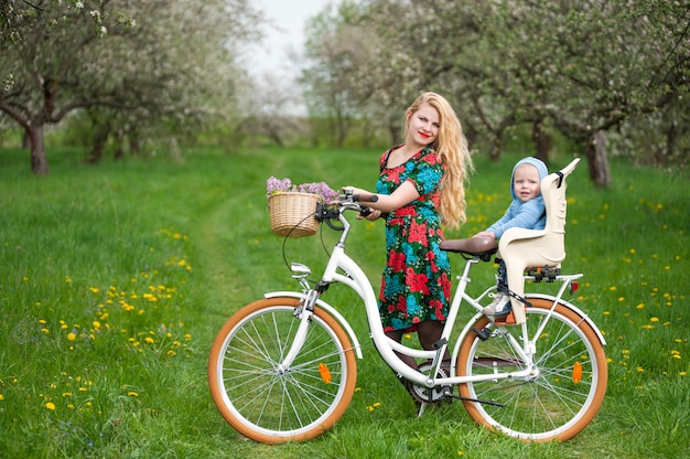 Femme blonde avec vélo de ville avec bébé dans la chaise de vélo