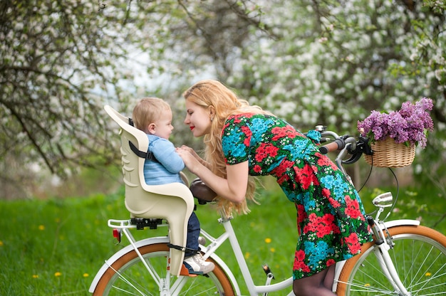 Photo femme blonde avec vélo de ville avec bébé dans une chaise de vélo