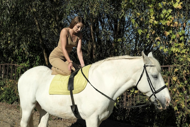 Une femme blonde en vêtements légers fait du yoga sur un cheval à l'extérieur