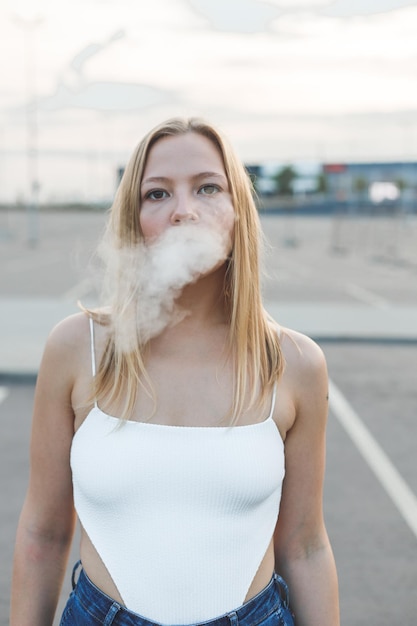 Photo une femme blonde en ville avec un cigare électronique.