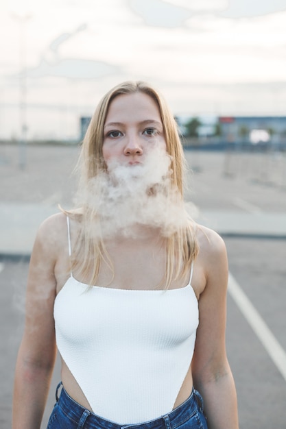 Femme blonde en ville avec vapotage de cigares électroniques