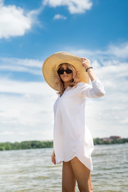 Femme en blouse blanche et chapeau de paille reposant sur une chaude journée d'été marchant sur le lac