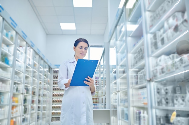 Femme en blouse blanche avec dossier en pharmacie