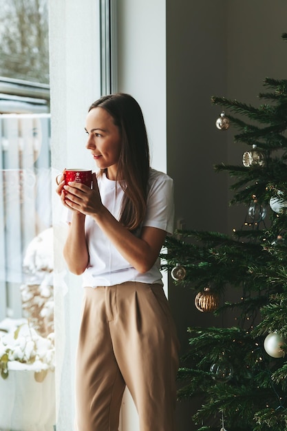 Femme avec boisson chaude près de sapin de Noël