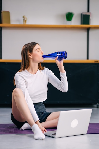 Une femme boit de l'eau après un exercice intense à la maison