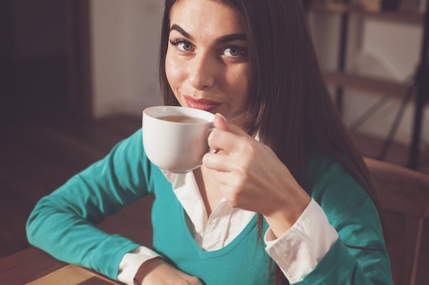 La femme boit une tasse de café à la table en bois