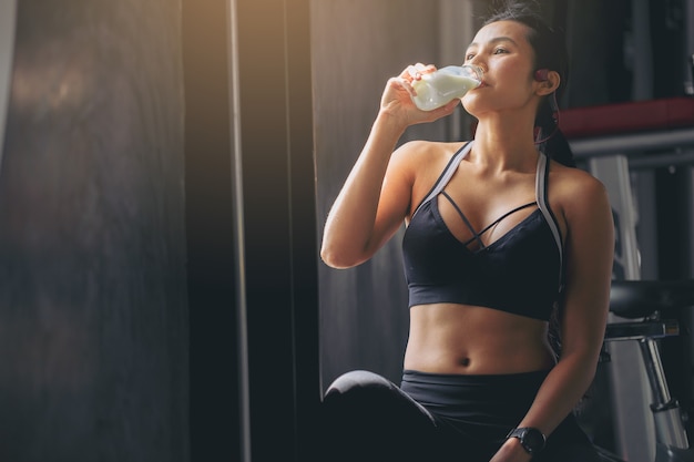 Femme de bonheur en tenue de sport buvant un milkshake en poudre de protéine après l'entraînement à la salle de fitness