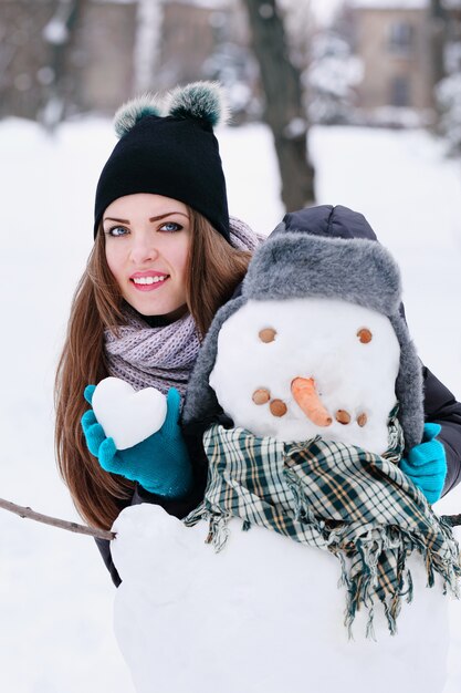 Femme avec un bonhomme de neige et une boule de neige en forme de coeur