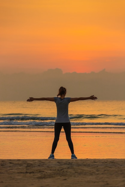 Femme en bonne forme debout et faire de l'exercice sur la plage le matin avec un ciel coloré en arrière-plan.